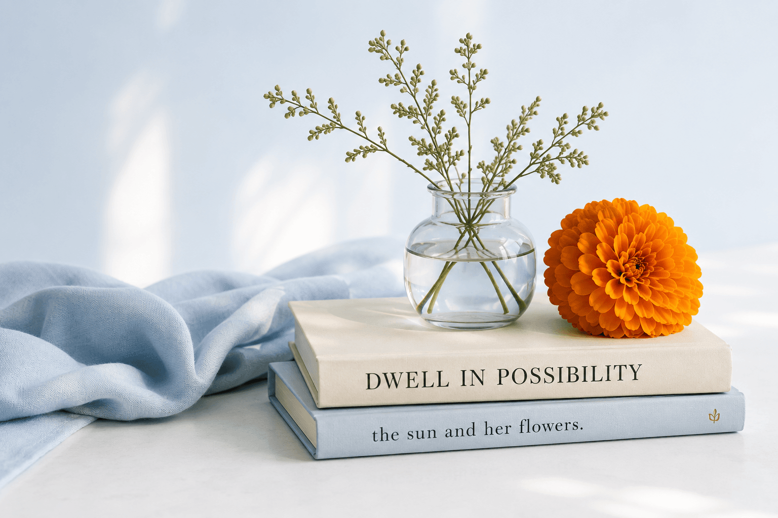 A soft still-life of a marigold in a glass vase resting on books with powder blue fabric